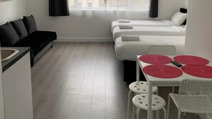 Et lille hotelværelse med tekøkken, seng, sofa og spiseplads med bord og stole.