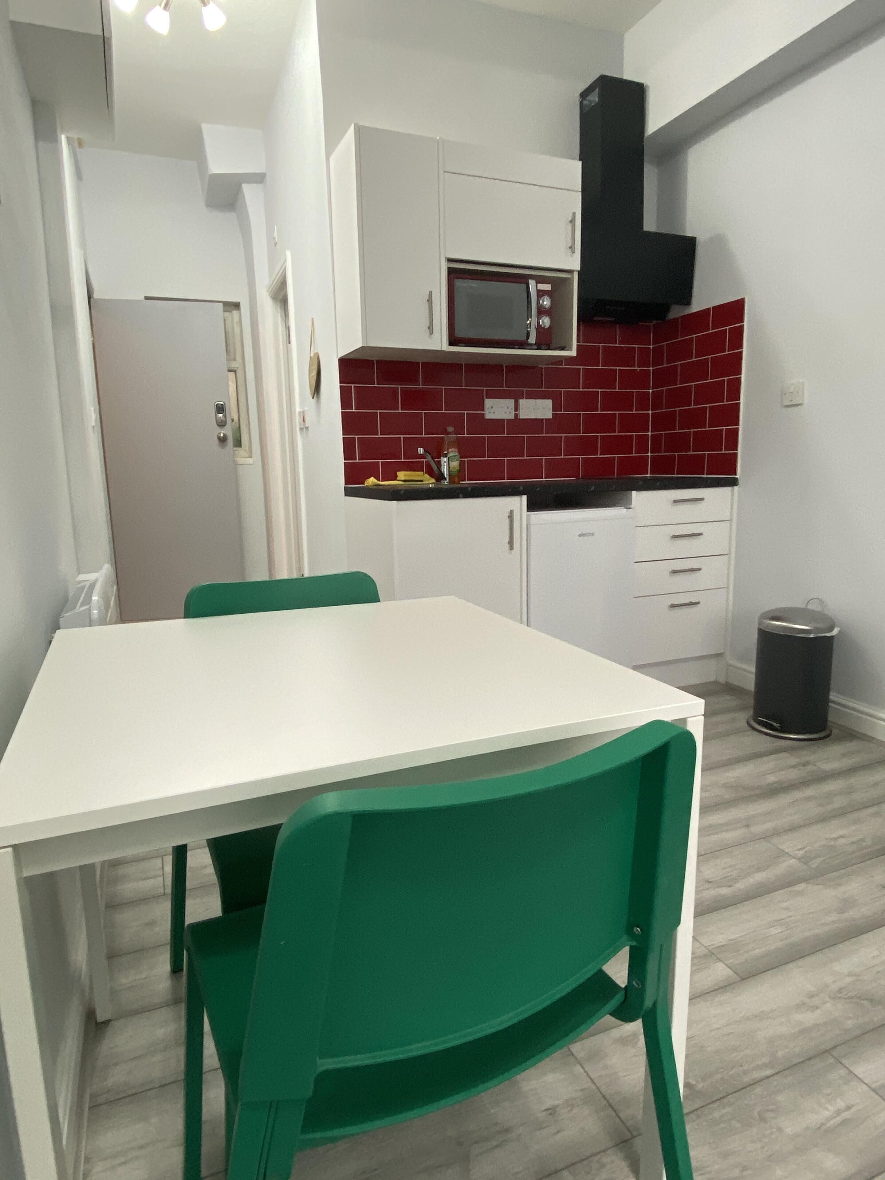 A compact kitchen with white cabinets, a red-tiled backsplash, a microwave, and a trash can.