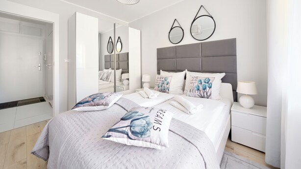 A modern bedroom with a large bed, bedside tables, a wardrobe, and a mirror. - Apartamenty Sun & Snow Blizej Morza (Kolobrzeg)