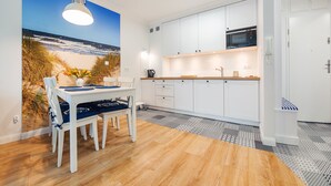 A modern kitchen with white cabinets, a microwave, and a dining area with a beach mural. - Apartamenty Sun & Snow Blizej Morza (Kolobrzeg)