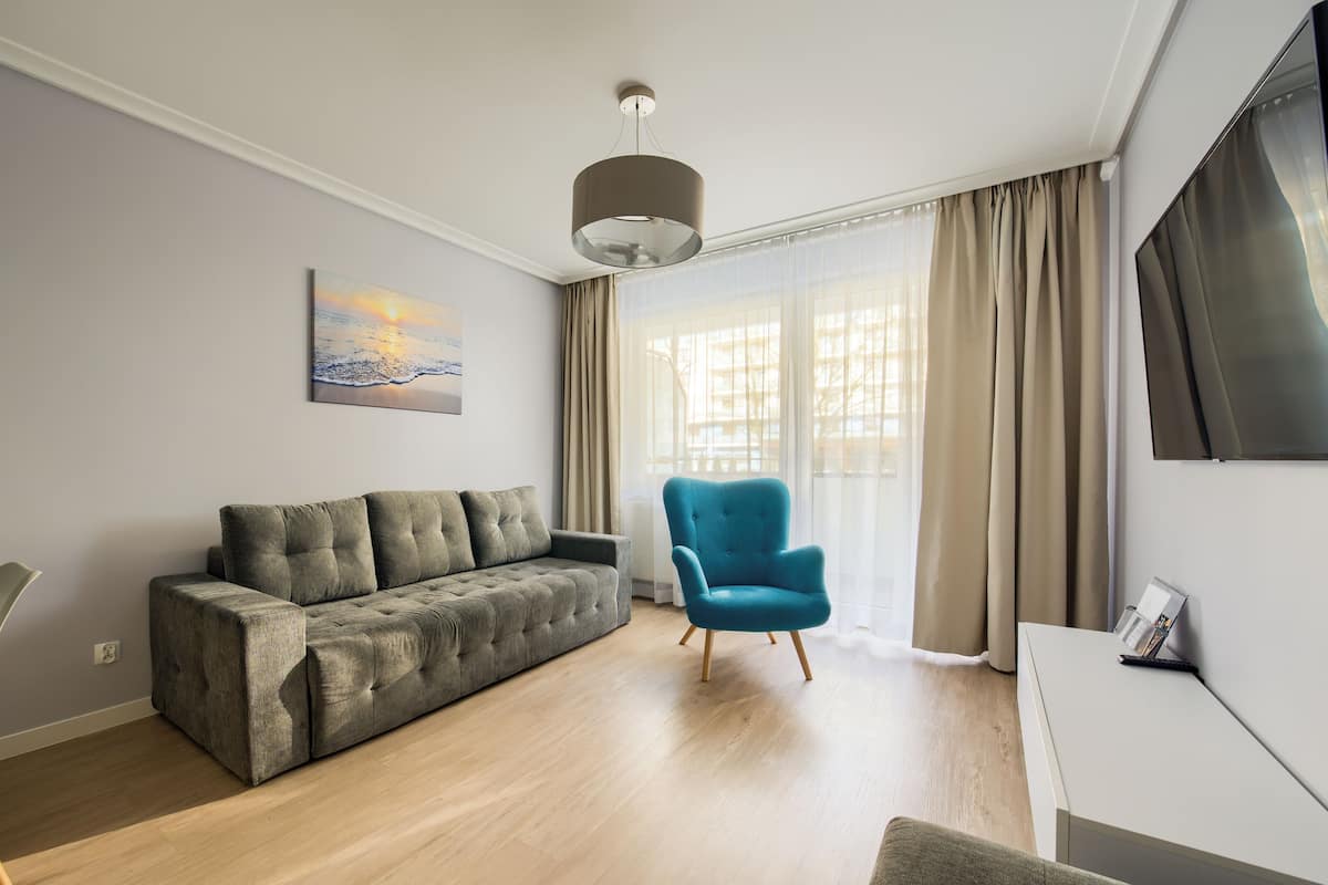 Ein modernes Wohnzimmer mit grauem Sofa, blauem Sessel, Flachbildfernseher und einem Bild an der Wand.