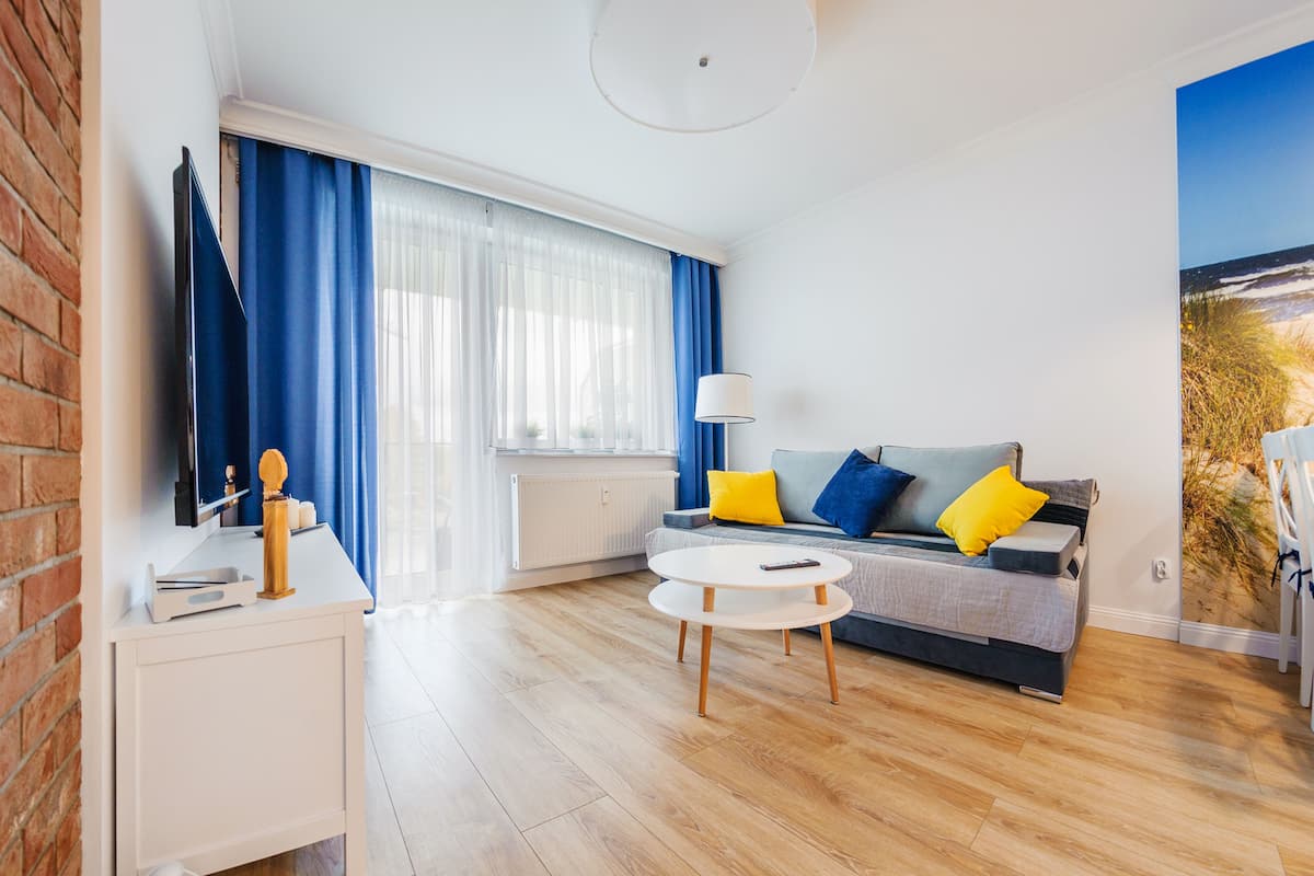 Ein modernes Wohnzimmer mit einer Couch, einem Couchtisch und einem Fernseher auf einem Standfuß.