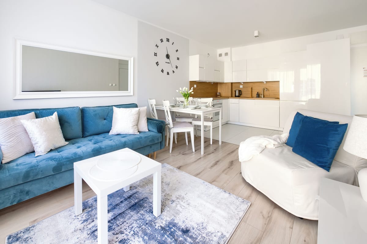 Ein modernes Wohnzimmer mit einem blauen Sofa, einem weißen Couchtisch und einem Essbereich mit weißen Stühlen und einem Holztisch.