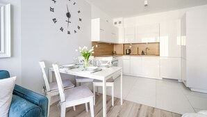A modern kitchen with white cabinets, a wooden countertop, and a dining area with a white table and chairs. - Apartamenty Sun & Snow Blizej Morza (Kolobrzeg)