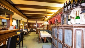 A restaurant interior with wooden beams, tables, chairs, and a bar area with bottles. - Hotel Vanda (Irschen)