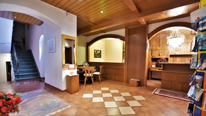 A spacious living area with a checkered floor, wooden beams on the ceiling, a staircase, and a kitchen area with wooden cabinets. - Hotel Vanda (Irschen)