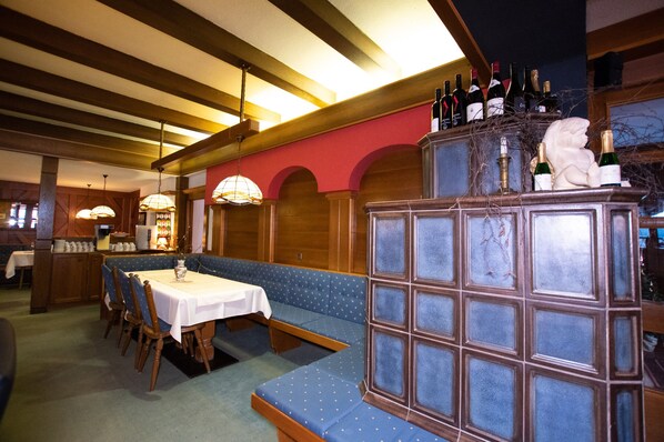 A restaurant with a long wooden bench seating area, a high counter with bottles, and a red wall.