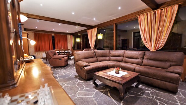 A spacious living area with a large brown leather sectional sofa, a wooden coffee table, and a chessboard on a stone-patterned floor. - Hotel Vanda (Irschen)
