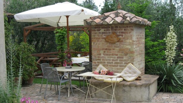 Un patio al aire libre con pared de ladrillo, pérgola de madera y una mesa con sillas.