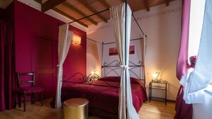 Un dormitorio con una cama con dosel, una mesita redonda dorada y una butaca tapizada de rojo.