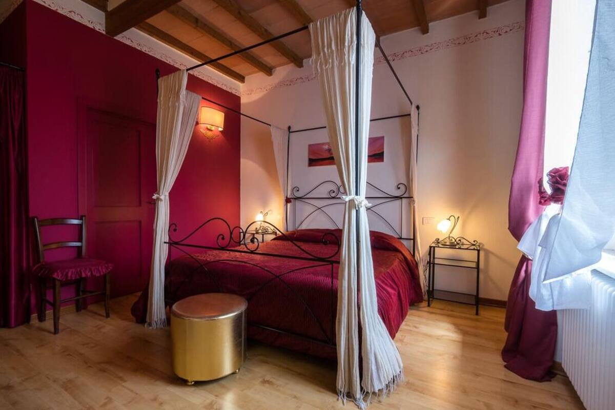 Un dormitorio con una cama con dosel, una mesita redonda dorada y una butaca tapizada de rojo.