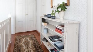 A hallway with a patterned rug, a white door marked '3', a white console table with books and a mirror, and a white wall with a subtle pattern.