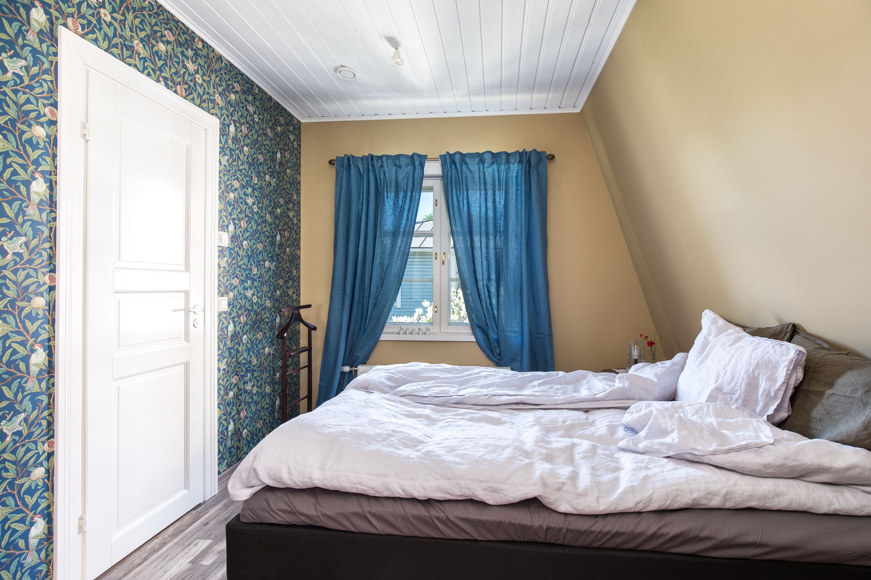 A bedroom with a bed, a window with blue curtains, and a door.