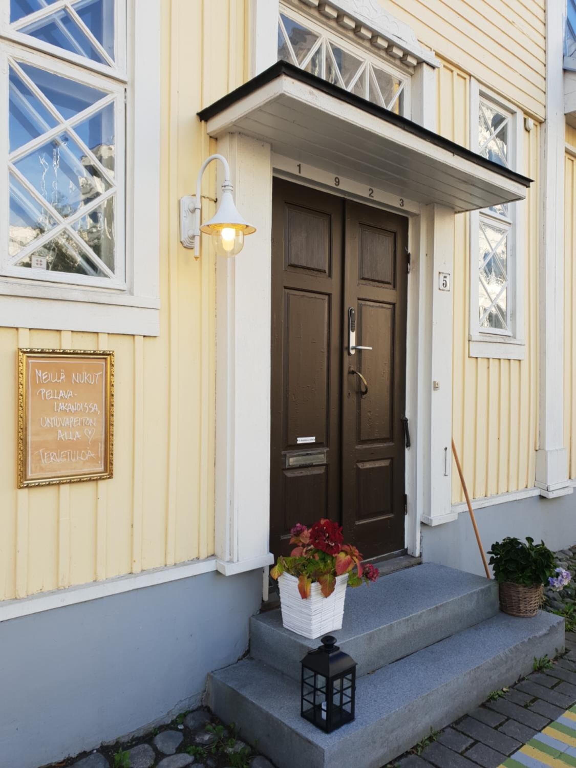 A building with a dark brown door, a light fixture above the door, and a sign on the wall.