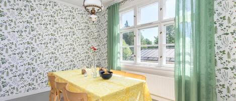 A dining area with a table set for four, a hanging light fixture, and a window with green curtains.