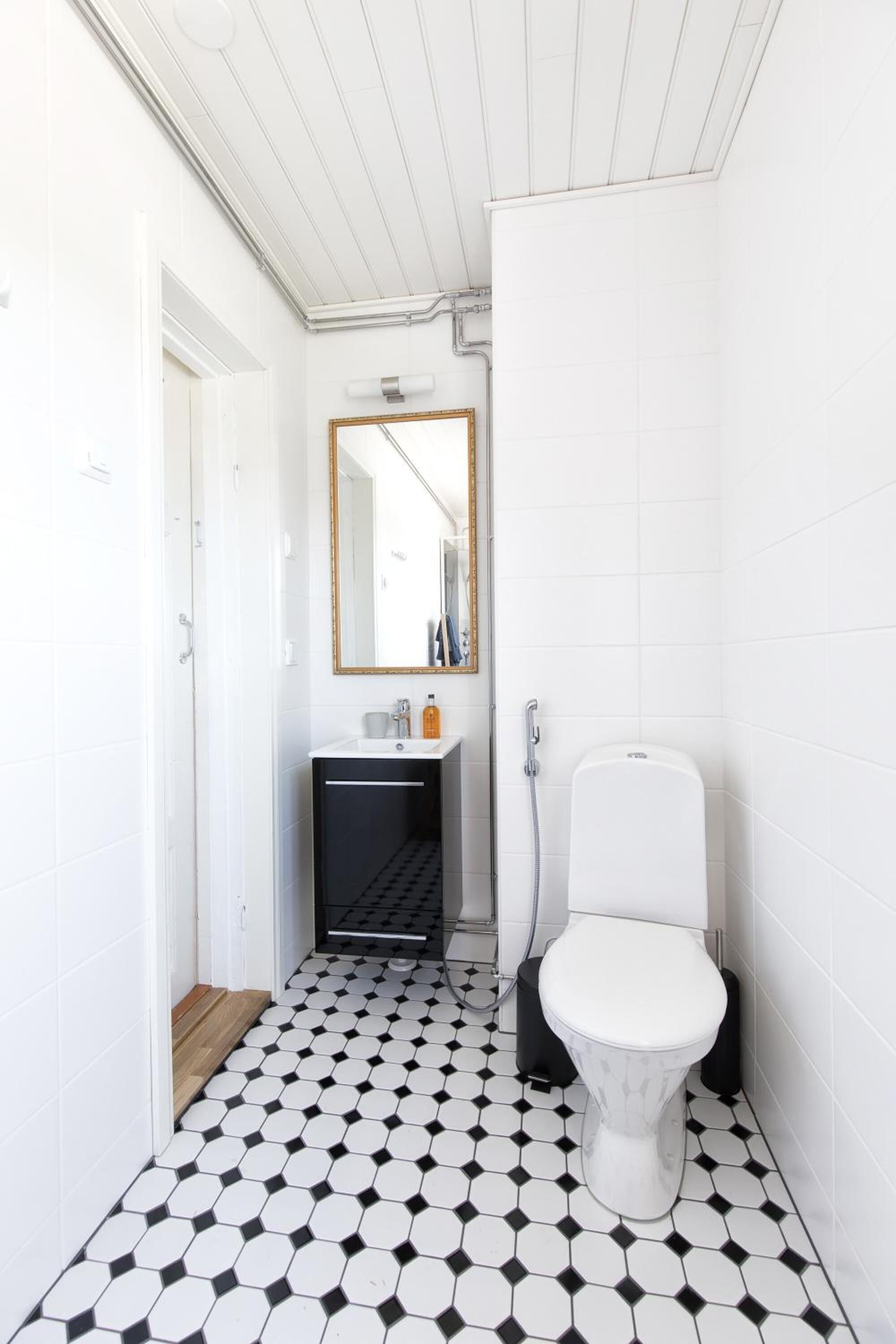 A bathroom with a white toilet, a sink, and a mirror. The floor has a black and white hexagonal tile pattern.