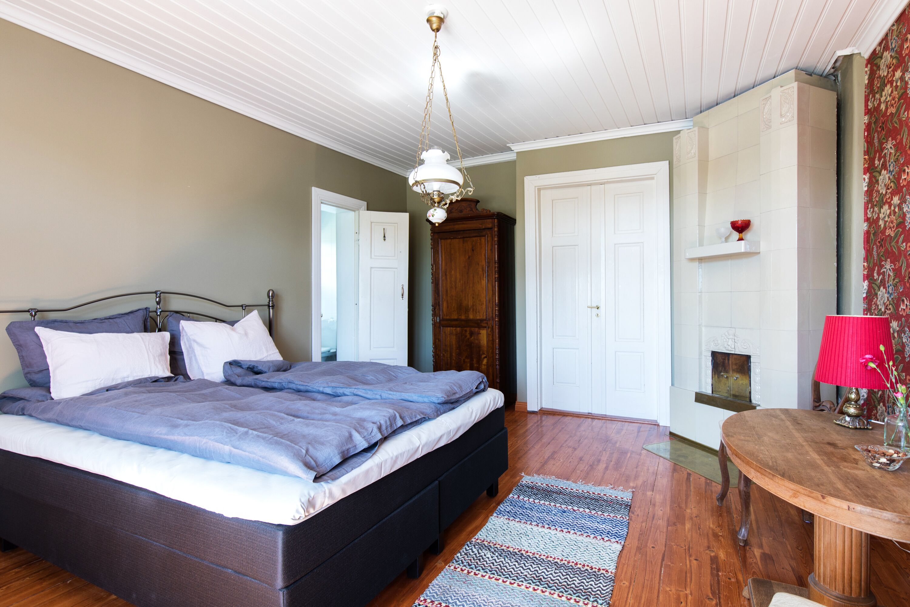 A bedroom with a bed, wooden wardrobe, white doors, and a fireplace.