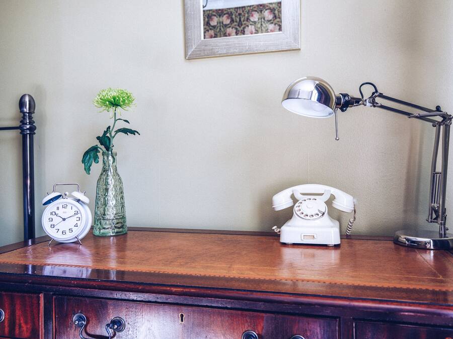 A wooden desk with a vintage alarm clock, a telephone, and a lamp.