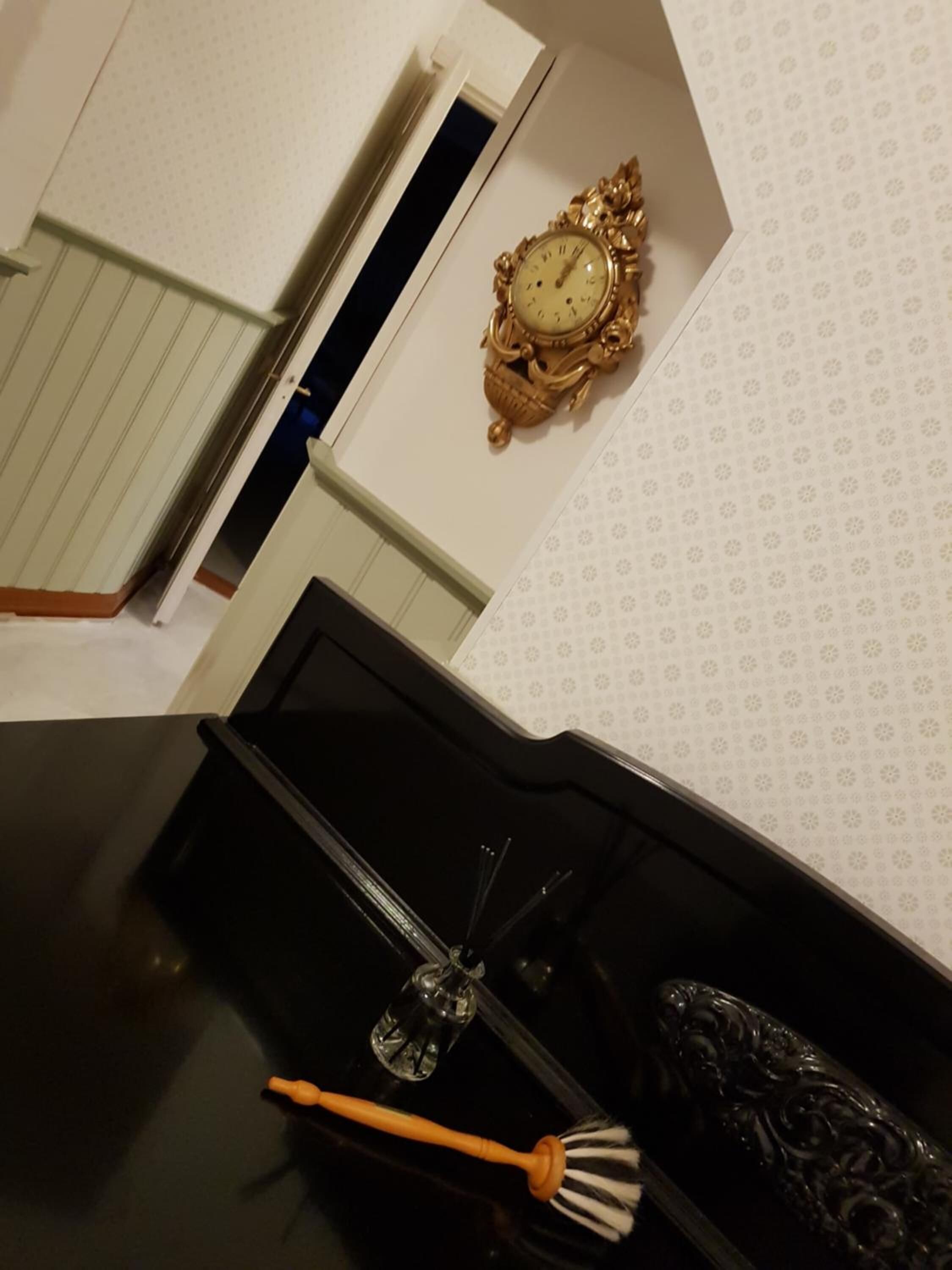 Un baño con tocador negro, un reloj dorado decorativo en la pared y un papel tapiz estampado.