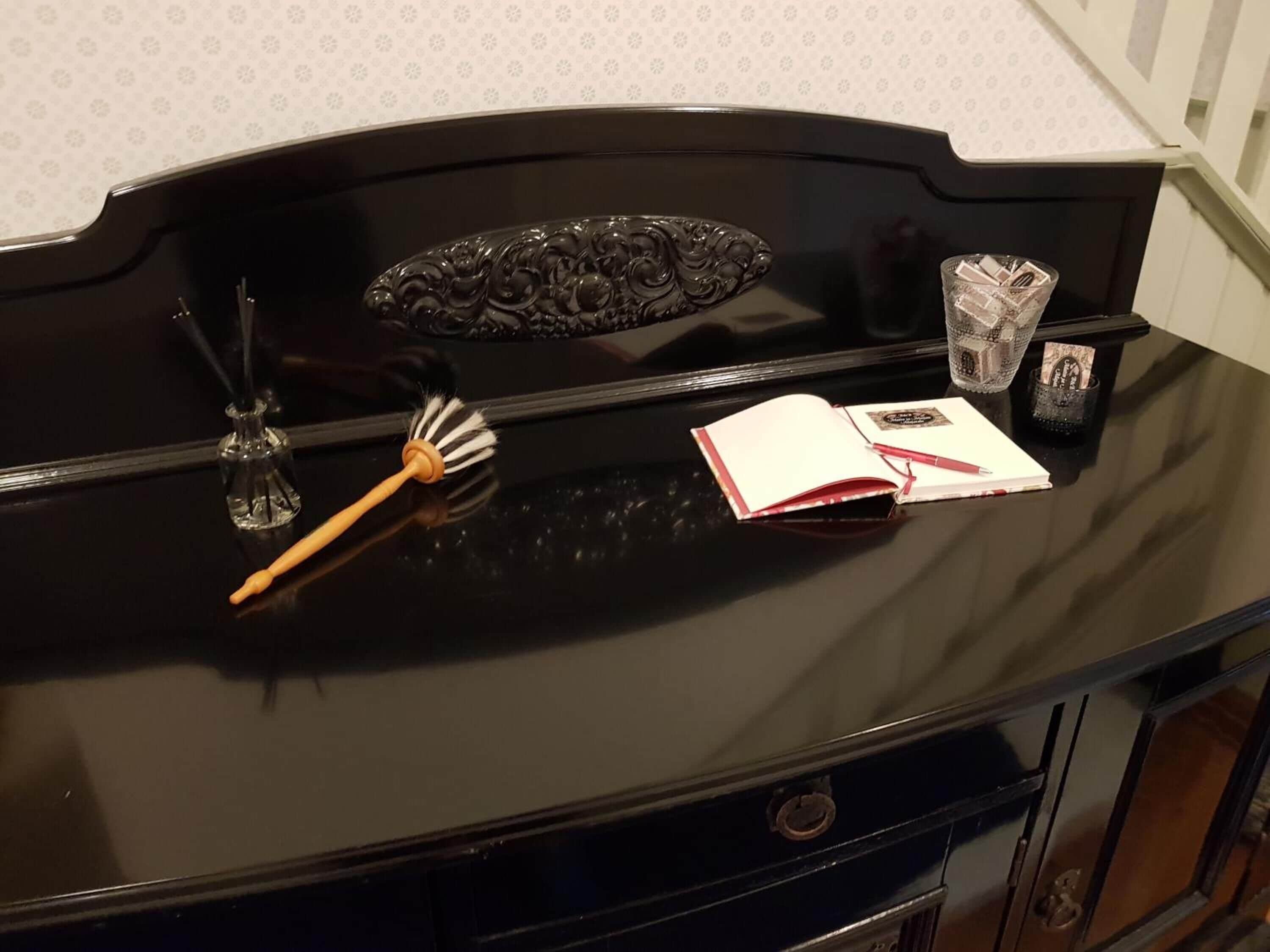 A black piano with a decorative design on the front, a book, a pen, and a glass with a decorative item on a table.