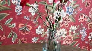 A clear glass vase with flowers on a wooden surface against a floral wallpaper background.