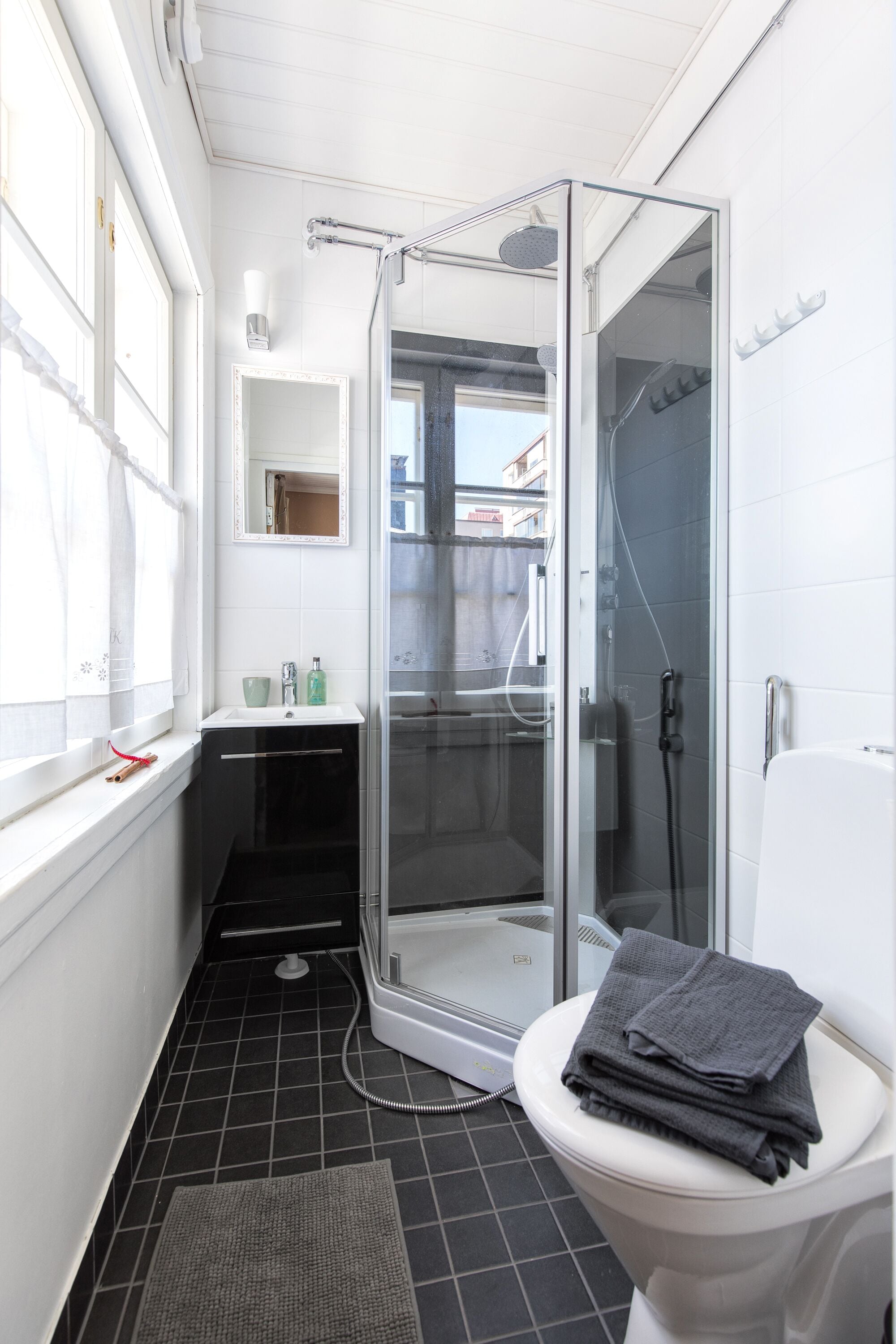 A bathroom with a glass-enclosed shower, a white toilet, a sink with a mirror, and a window with curtains.