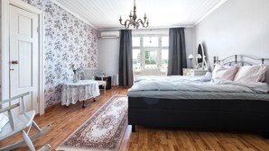 A bedroom with a large bed, a chandelier, a desk, and a window with curtains.