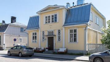A two-story building with a yellow facade, a dark blue roof, and a front porch with seating.