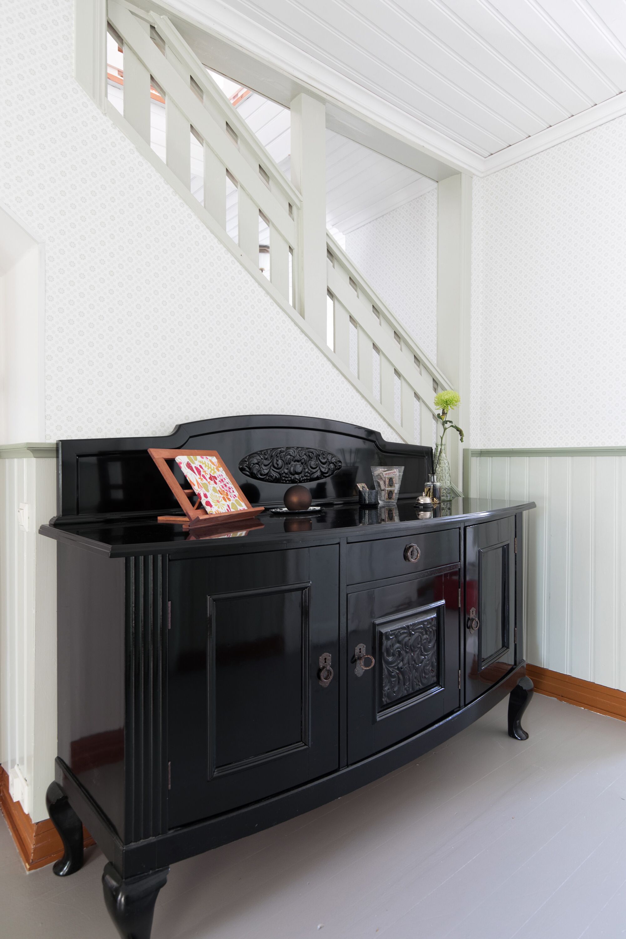 Un mobiletti in legno nero con una cornice, un vaso con un fiore e un oggetto decorativo sopra.