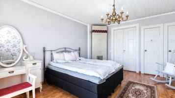 Een slaapkamer met een bed, een bureau, een stoel, een schommelstoel, een kroonluchter en een spiegel.
