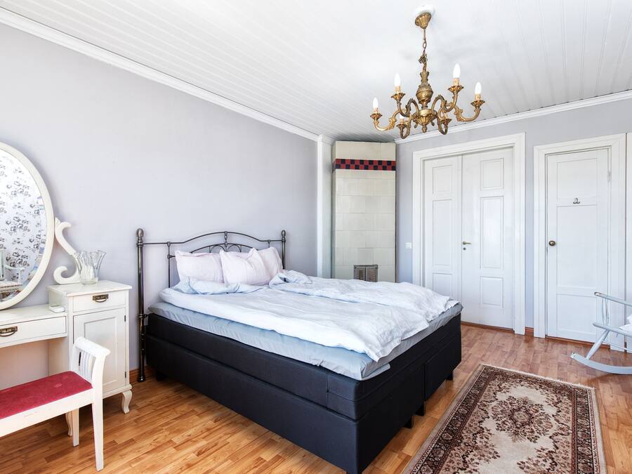 Een slaapkamer met een bed, een bureau, een stoel, een schommelstoel, een kroonluchter en een spiegel.