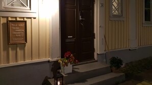 A building with a dark wooden door, a lit wall-mounted light, and a sign with text.
