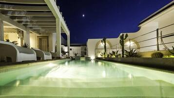 Relax by the pool, surrounded by a covered seating area and a staircase leading to an upper level with a balcony overlooking the water.