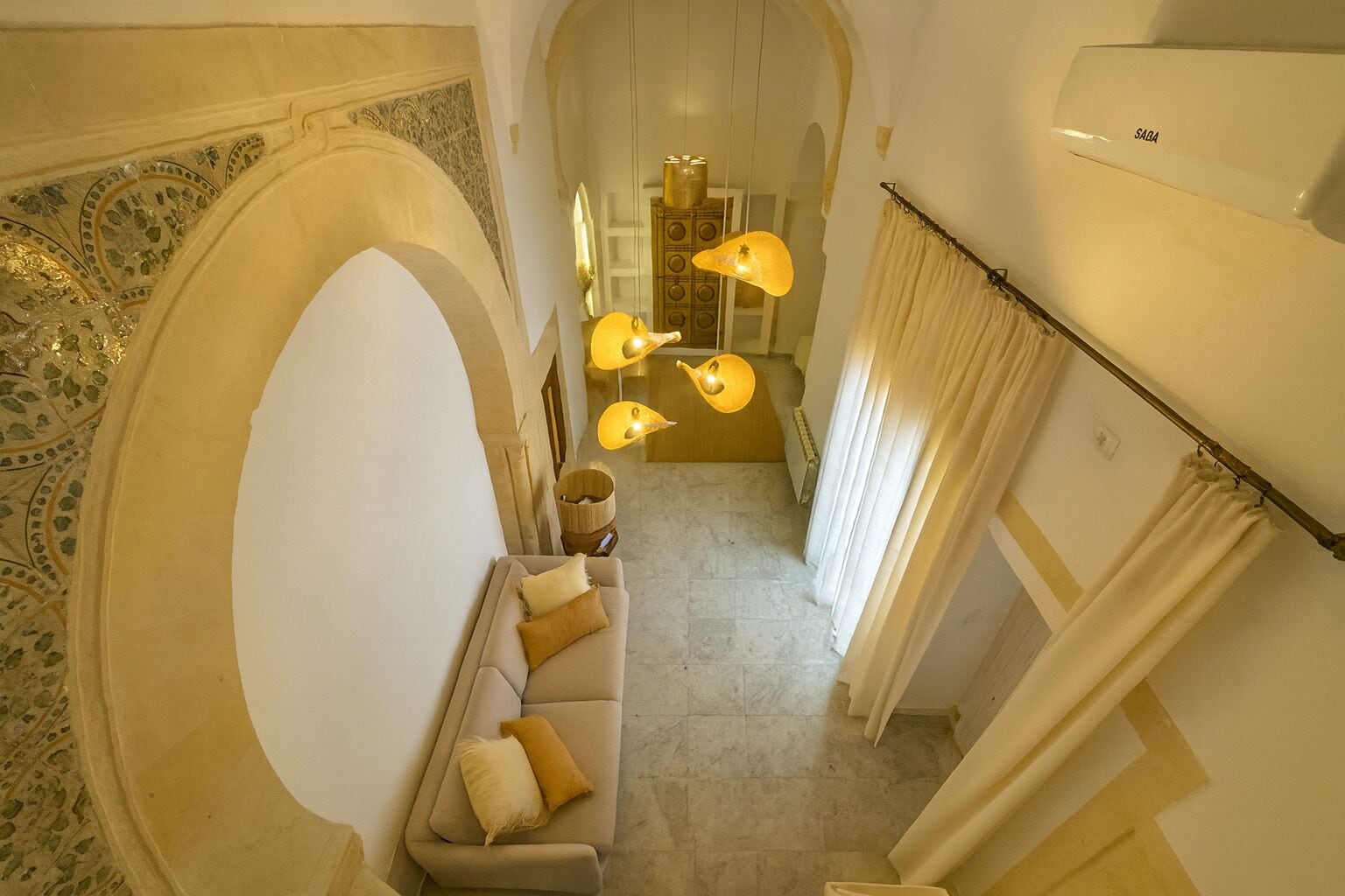 Um corredor com um sofá, luminárias decorativas e um ventilador de teto.