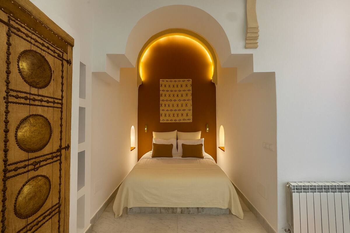 A bedroom with a bed centered under a large, illuminated archway.
