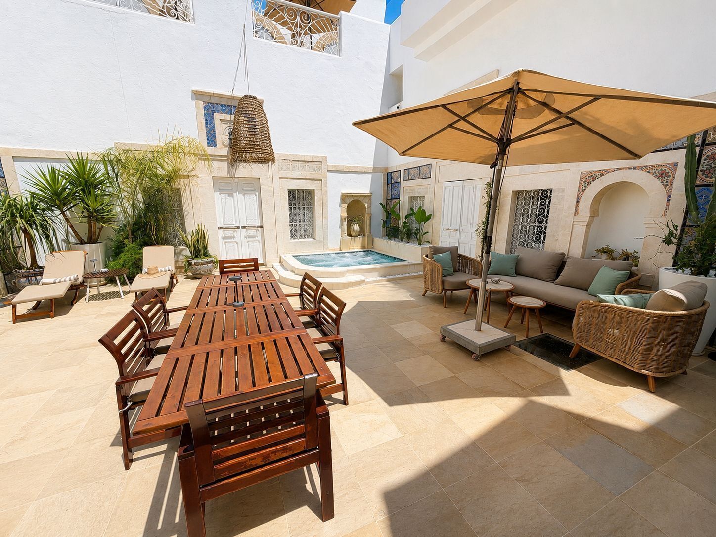 A courtyard with a wooden table, chairs, a sofa, and an umbrella.