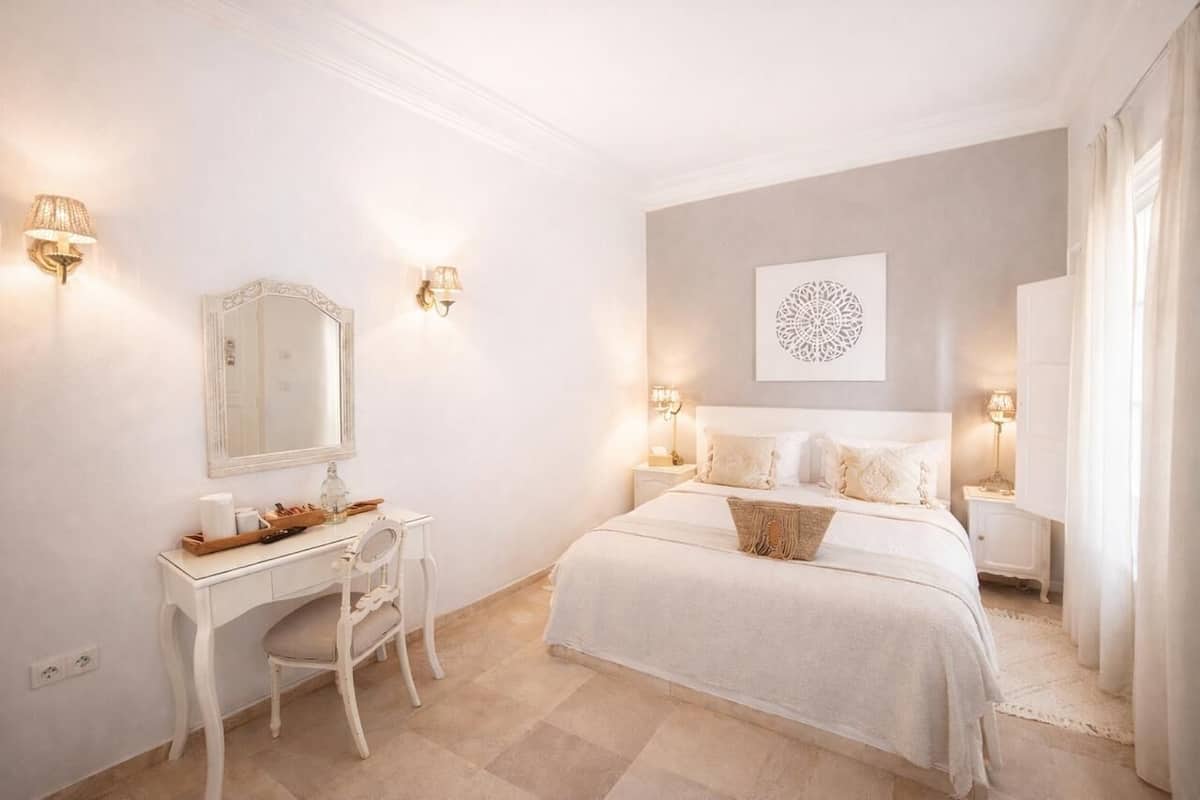 A bedroom with a bed, a desk, and two wall-mounted lamps.