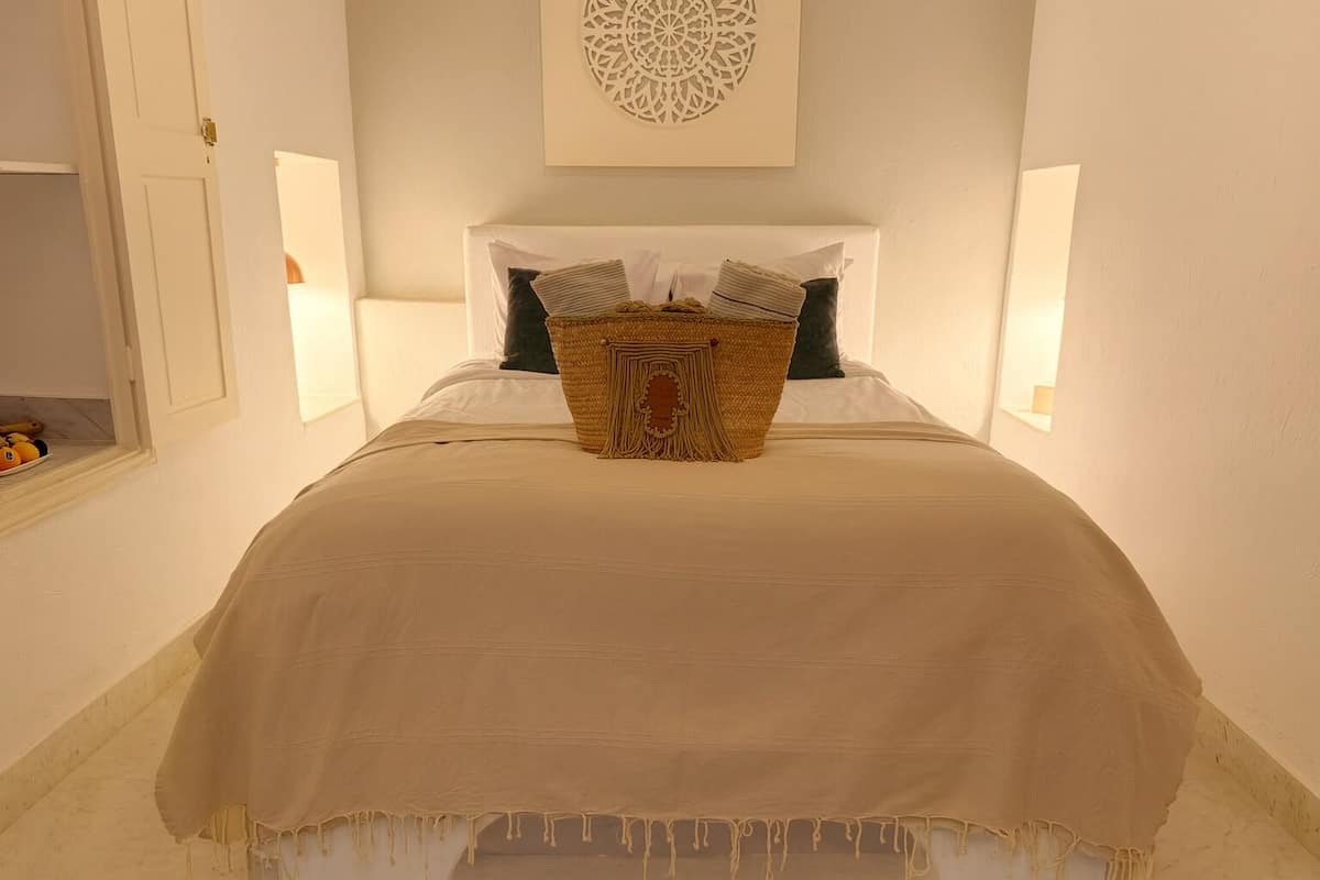 A neatly made bed with a beige bedspread and a decorative basket on the headboard.