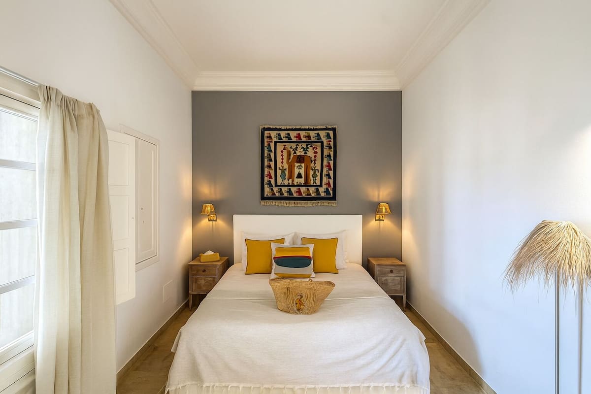 A bedroom with a bed, two bedside tables, a wall-mounted artwork, and a window with curtains.