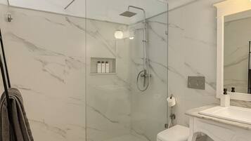 A modern bathroom with a glass-enclosed shower, a white toilet, and a vanity with a mirror.
