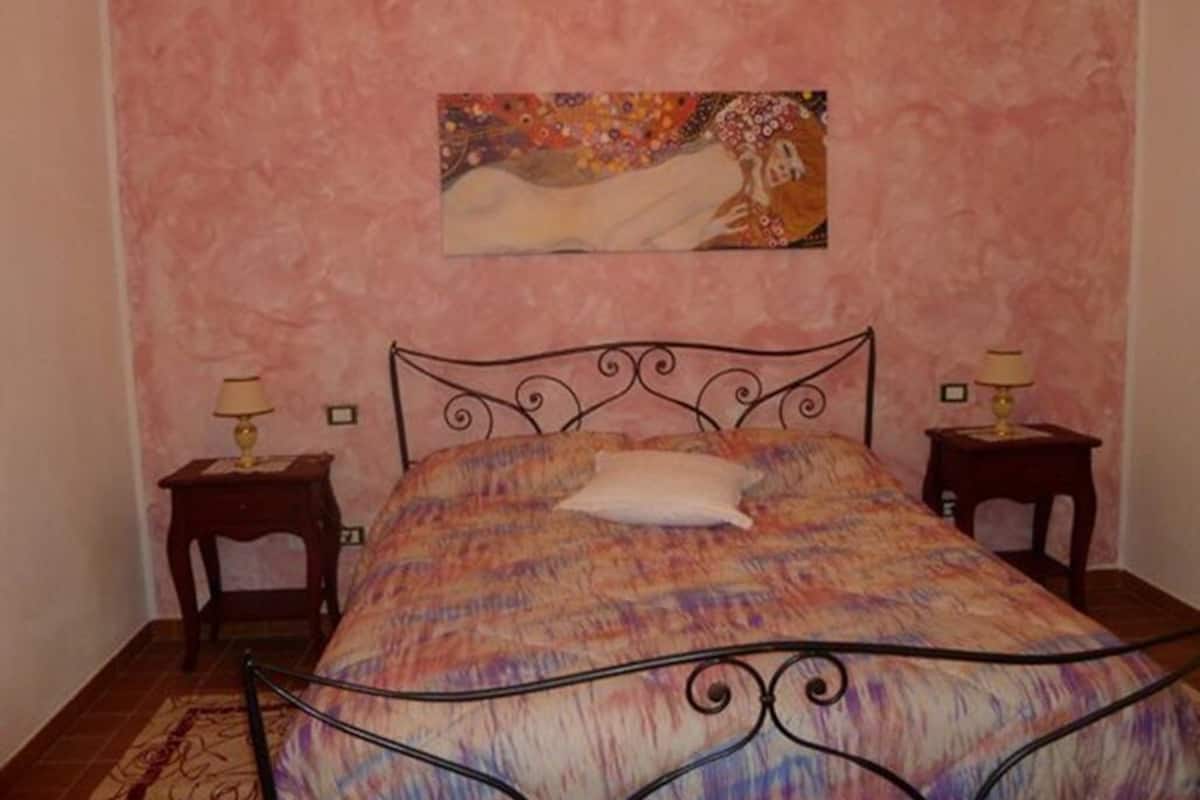 Une chambre à coucher avec un lit, deux tables de chevet, un tableau au mur et un tapis à motifs.