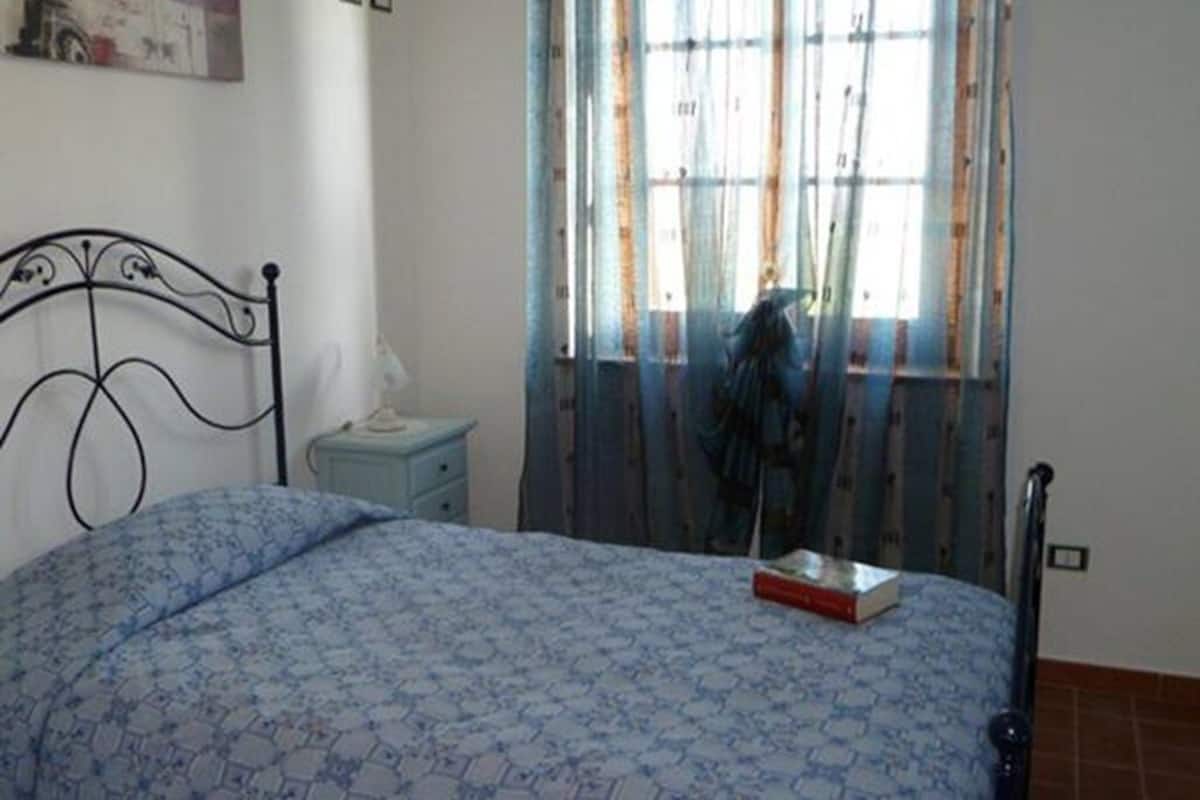 Une chambre à coucher comprenant un lit, une table de chevet, une fenêtre avec des rideaux et un interrupteur fixé au mur.