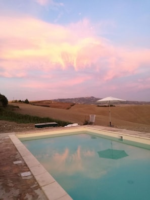 Une piscine offrant une vue dégagée sur le paysage environnant, avec ses collines ondoyantes et le ciel au coucher du soleil.