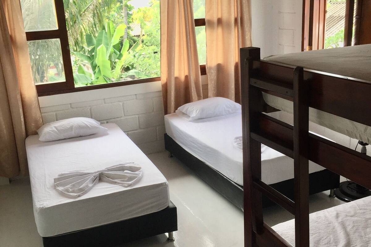 A room with two beds, a bunk bed, and a window with curtains.