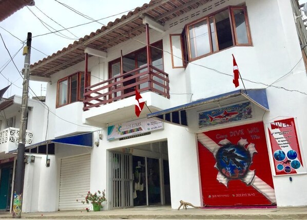 A two-story building with a white facade, a balcony with red railings, and a storefront with a red and blue advertisement. - Casa Hotel Los Kunas (Acandi)