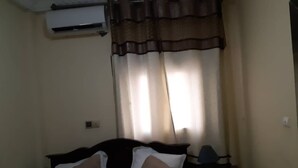 A hotel room with a bed, a nightstand, and a window with curtains. - Residence MB Meublee (Douala)