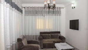 A living room with a sofa set, a TV mounted on the wall, and a table with a white tablecloth. - Residence MB Meublee (Douala)