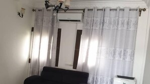 A living room with a black sofa, a smaller armchair, a coffee table, and a white refrigerator. - Residence MB Meublee (Douala)