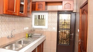 A kitchen with wooden cabinets, a stainless steel sink, and a window with a metal grill. - Residence MB Meublee (Douala)