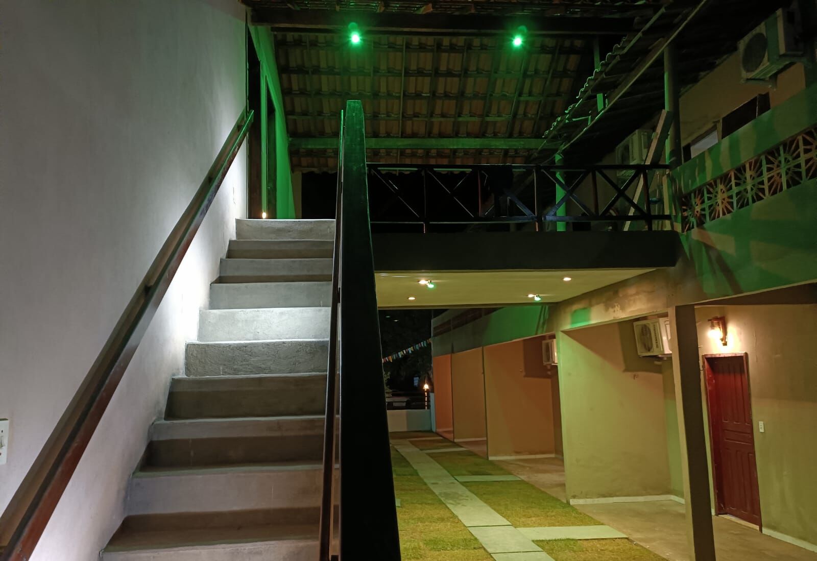 Una escalera con barandilla metálica que sube a un área del segundo piso, con paredes verdes y una puerta roja.